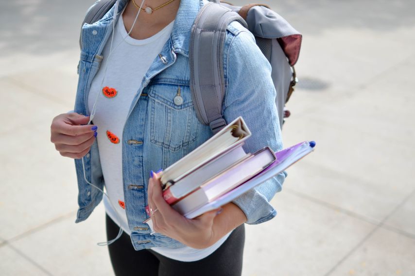 female student holding books wearing denim jacket and backpack