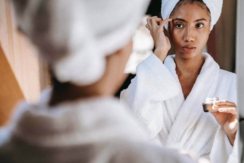 Woman applying collagen cream to face in mirror bathrobe