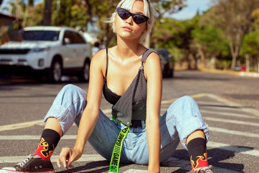Stylish young woman sitting on road wearing streetwear brands