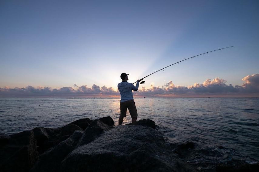 Man casting fshing rod from shore near water