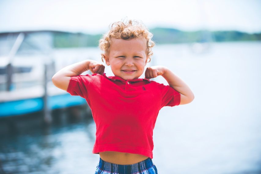  healthy young boy standing near dock flexing arms