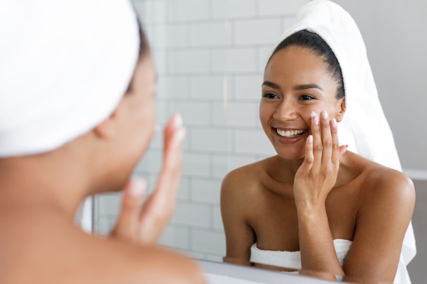 woman applying skincare product in bathroom wearing towel