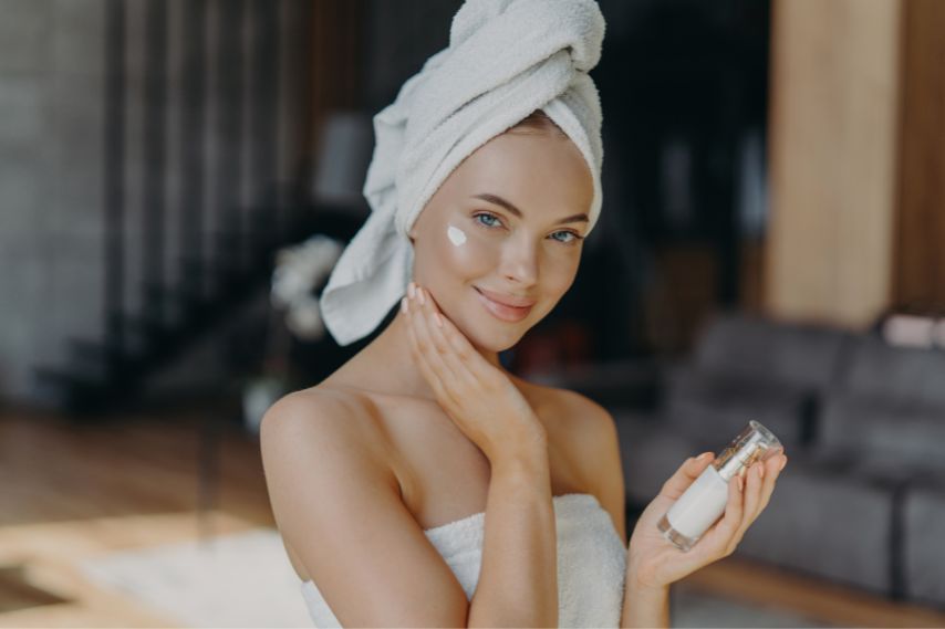 woman wearing towel applying skincare serum